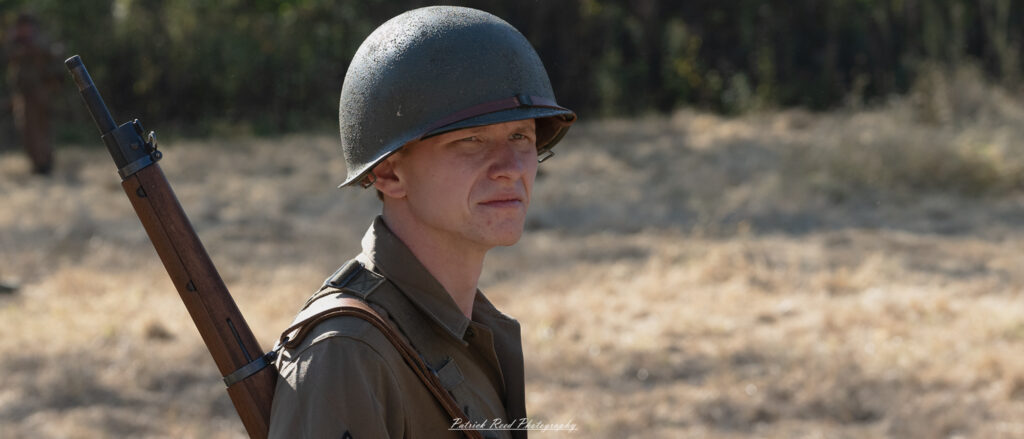 "Portrait of a U.S. GI (Government Issue) from the WWII era, dressed in a classic military uniform complete with insignia. The soldier stands confidently, showcasing a strong and determined expression, reflecting the spirit of the time. The backdrop features a subtle hint of the battlefield or military camp, adding context to his service. This image captures the resilience and bravery of American soldiers during the war."